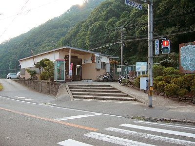 線路の向こうの山がすぐに迫った駅舎と赤信号の歩行者用信号機。