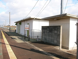 左に信号機室、右にトイレ。いずれも白いコンクリートの建物で無機質。トイレの入口の前にはブロック塀で作った壁が立てられている。