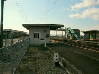 ホームから陸屋根の簡易な駅舎を真横に見て。少し遠くに跨線橋が写っている。