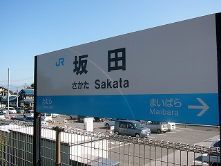 白い網の柵に沿うように立てられた長い二本足で立つJR西日本様式の「坂田」と書かれた駅名標。