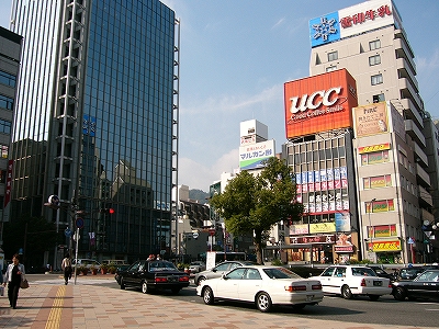 左に背の高いガラス張りの建物、右手に屋上広告のある背の低いビル群。