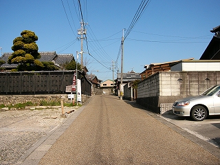 土色の細かい砂利をモルタルで固めた路面の坂道。電柱があり、両脇は住宅の様々な塀。