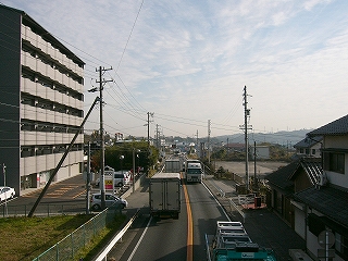 歩道橋から亀山方面に見た2車線の国道1号。大型トラックが何台も行き交っている。左手に7階建ての中規模マンション。