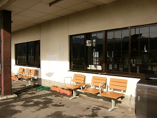 駅舎の建物の窓ガラスの枠の下に、薄茶色の一人掛け用の椅子が幾つか並んでいる。