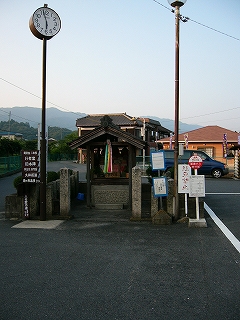 小さな祠と背の低いバス停、長い一本のポールで支えられた丸い時計のあるロータリー中心。