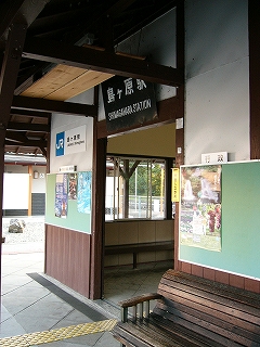 駅舎から出て、斜め右から駅舎入口を見て。黒い鉄板に白い字で「島ヶ原駅」とかかれたものが掲げられ、入口の両脇には鶯色の新しい掲示板が取り付けられている。