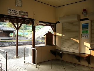 駅舎内。左にホームへの出口、右にシャッターの閉まった窓口を見て。軒と窓口の台は焦茶で、壁は白色。