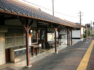 焦げ茶の柱に支えられた日本瓦の軒下。軒下の駅舎入口の両脇にはそれぞれ分別のための3つのステンレスのゴミ箱と木製のベンチが置いてある。