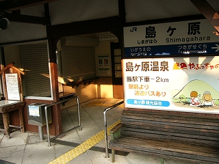 駅舎入口と木製のベンチ、その上に壁に取り付けられた島ヶ原温泉の宣伝看板と無灯式駅名標。