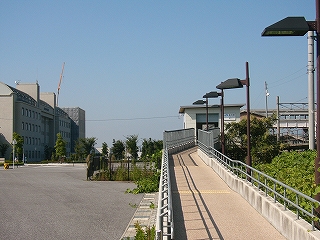 左手奥に縦に見る大学の建物、右手手前に簡易駅舎へのスロープ。