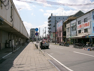 道路右脇に三階建ての古い建物が立ち並ぶ。左側には桜井線の高架。