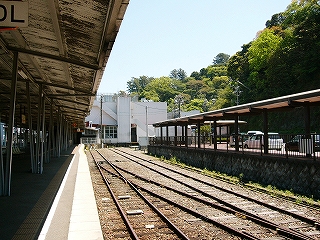 ２線が駅舎の白い壁の前で止まっている。その右は柵の向こうに屋根付きのタクシー乗り場のようなものがある。