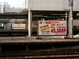左にホームに立てられた駅名標、右手に大きな横長の看板。