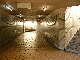 幅としては1.5車線程度の歩行者専用の地下道。幅としては広く、やや明るい。先の方は階段になっていて光差し込む出口があり、すぐ手前右にも同じように出口がある。