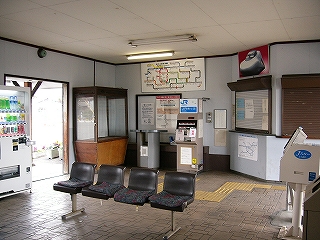 椅子、券売機、大型の飾りケースのある駅舎内。