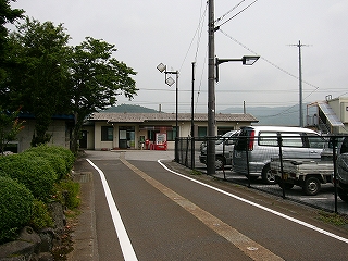 駅への細い道と遠くに駅舎、左は人家の背の低いつつじの垣根。